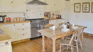 Une cuisine avec des meubles de rangement en bois, une cuisinière à gaz et une table à manger pour quatre personnes.