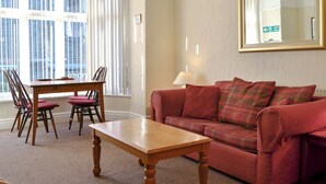 A living room with a wooden table, red sofa, and a large mirror on the wall. - 2 bedroom accommodation in Keswick (Keswick)