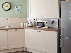 A kitchen with white cabinets, a microwave, a kettle, and a refrigerator.