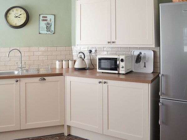 A kitchen with white cabinets, a microwave, a kettle, and a refrigerator.
