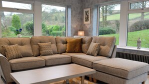 A sectional sofa with patterned cushions, a coffee table, and a view of a green landscape through large windows.