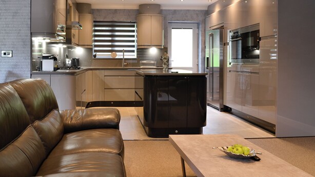 A modern kitchen with stainless steel appliances, a leather sofa, and a dining table with fruit.