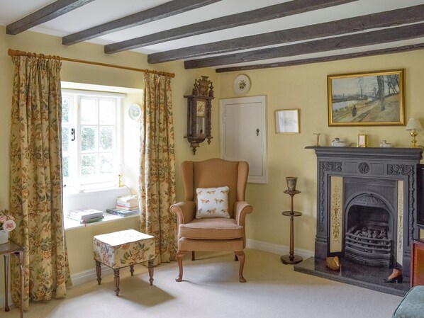 A room with a traditional fireplace, a wooden chair with a cushion, a small table, and a window with curtains. - 3 bedroom accommodation in Sinnington, near Pickering (Sinnington, near Pickering)