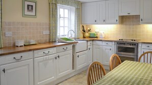 A kitchen with white cabinets, a tiled backsplash, a window with curtains, a sink, a stove, and a table with chairs.