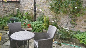 A patio area with wicker furniture, a stone wall, and a variety of plants and flowers.
