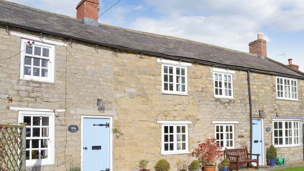 A stone building with multiple windows and doors, a small garden with potted plants, and a bench outside.