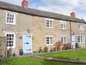 A stone building with multiple windows and doors, a small garden with potted plants, and a bench outside. - 3 bedroom accommodation in Sinnington, near Pickering (Sinnington, near Pickering)