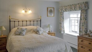 A bedroom with a bed, two bedside tables, a nightstand, a window with curtains, and a wall-mounted light fixture.