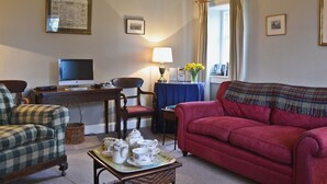 A living room with a television, a desk with a computer, a red sofa, a plaid blanket, and a table with tea set.