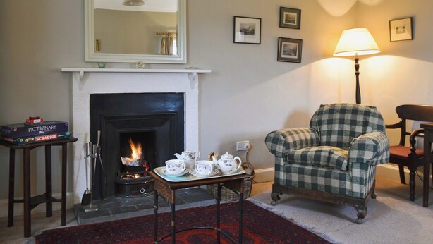 A cozy living room with a fireplace, a checkered armchair, a table with tea set, and a lamp.