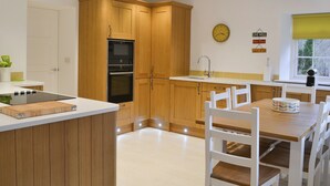 Una cocina moderna con armarios de madera, horno empotrado, microondas y un comedor con mesa de madera y sillas blancas.