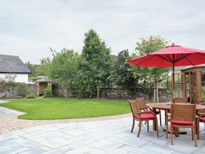 Een terras met een tafel, stoelen, een rode parasol en een stenen muur.