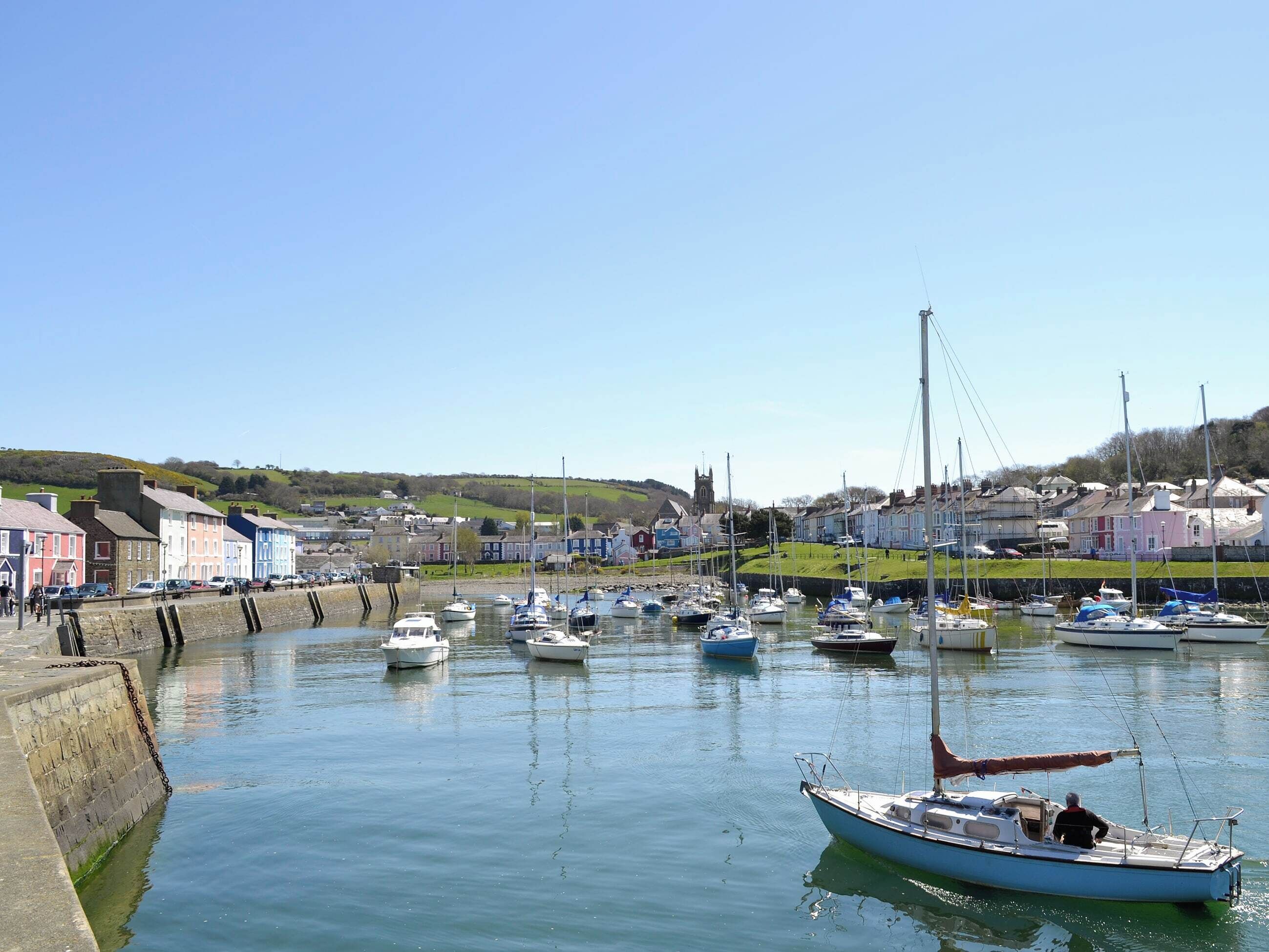 Un port où sont amarrés des bateaux, une église et des maisons aux couleurs vives qui bordent le quai.