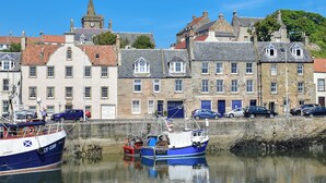 A harbor with boats docked, a stone building with multiple windows, and a clock tower in the background.