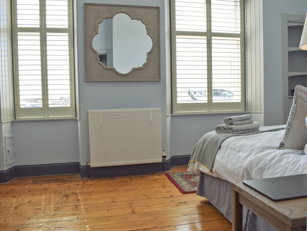 A bedroom with a bed, a laptop, a radiator, and a window with blinds.