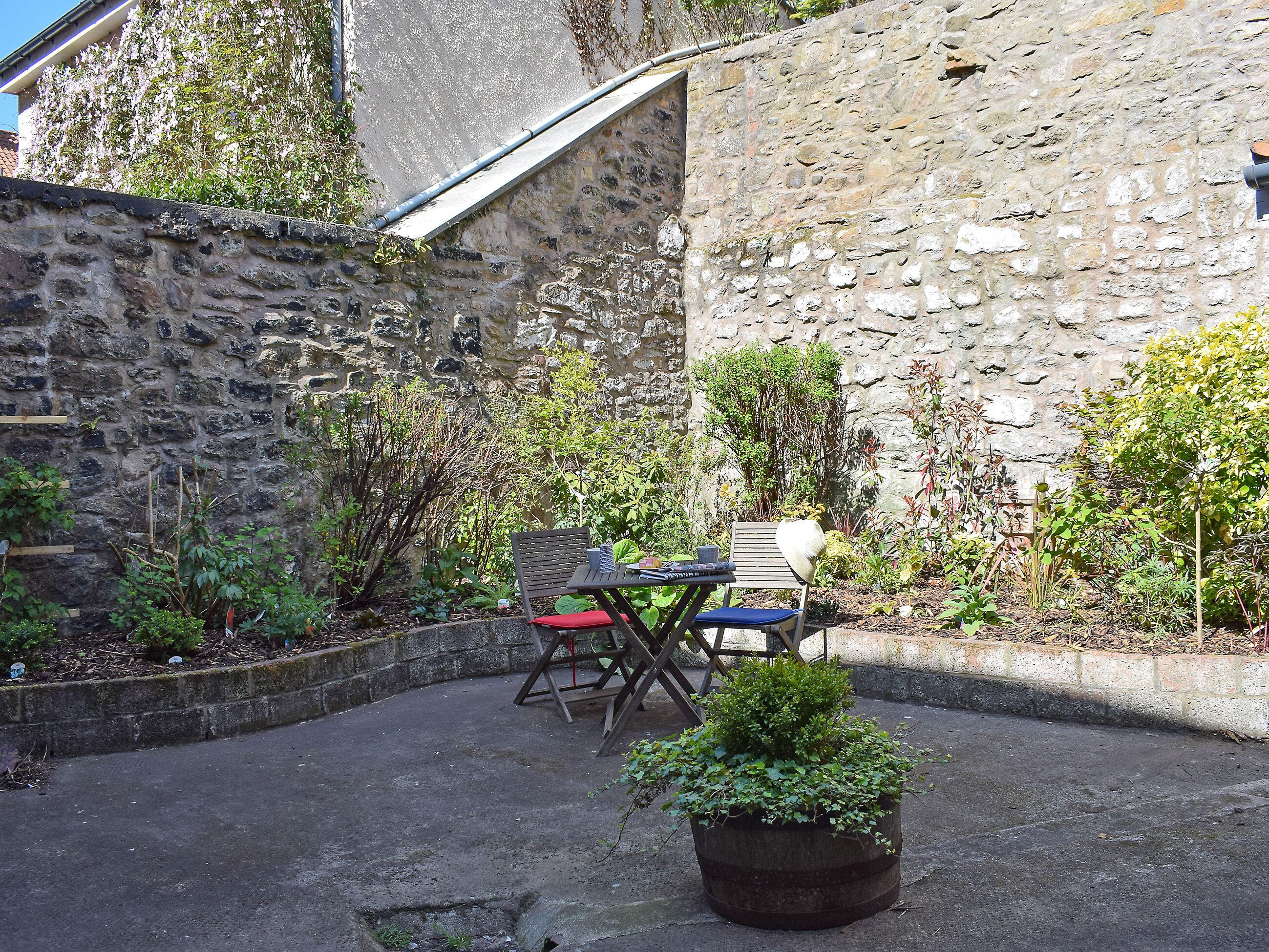 A stone wall, a small table with chairs, and a potted plant in a courtyard.