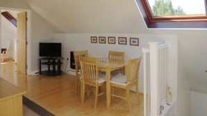 A dining area with a table and chairs, a television, and framed pictures on the wall. - 1 bedroom accommodation in Upton (Upton)