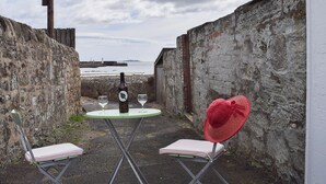 A small outdoor seating area with a table, two chairs, a bottle of wine, and a red hat.
