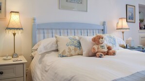 A neatly made bed with a teddy bear, two bedside lamps, and a framed picture on the wall.