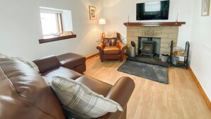 Una sala de estar con un sofá de cuero, chimenea, televisor y ventana.