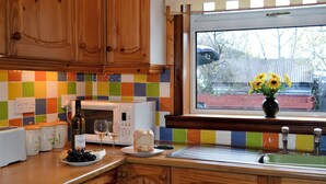 Una cocina con armarios de madera, un salpicadero de azulejos coloridos, un microondas, un lavamanos y un florero con flores en el alféizar.