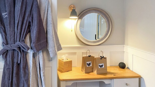 Un baño con tocador de madera, un espejo, una bata y dos bolsas de regalo.