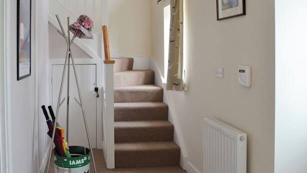 A staircase with carpeted steps, a radiator, a door with a coat rack, and a bucket with cleaning tools.