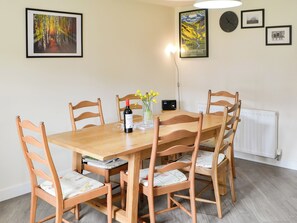 A dining area with a wooden table and chairs, a wine bottle, a vase with flowers, and framed pictures on the wall.