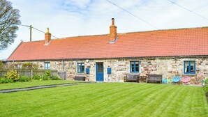 A stone house with a red-tiled roof, a front door, and a small porch with outdoor seating.