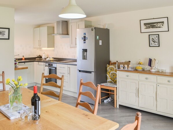A modern kitchen with white cabinets, a stainless steel refrigerator, and a dining table with chairs.