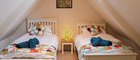 Une chambre avec deux lits, une petite table de chevet avec une lampe, une bande dessinée encadrée accrochée au mur et un plafond en pente.