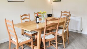 A dining area with a wooden table and chairs, a wine bottle, a vase with flowers, and framed pictures on the wall.
