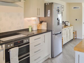 A modern kitchen with a stainless steel refrigerator, an oven, and a microwave. There are white cabinets with silver handles, a black countertop, and a wooden stool.