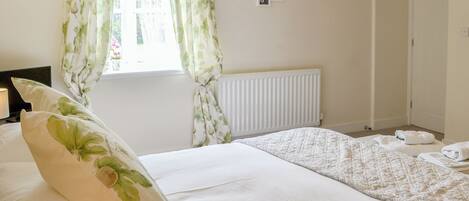A bedroom with a bed, a radiator, a window with curtains, and a wall with framed pictures.