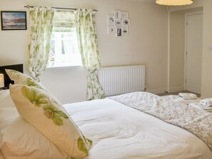 A bedroom with a bed, a radiator, a window with curtains, and a wall with framed pictures.