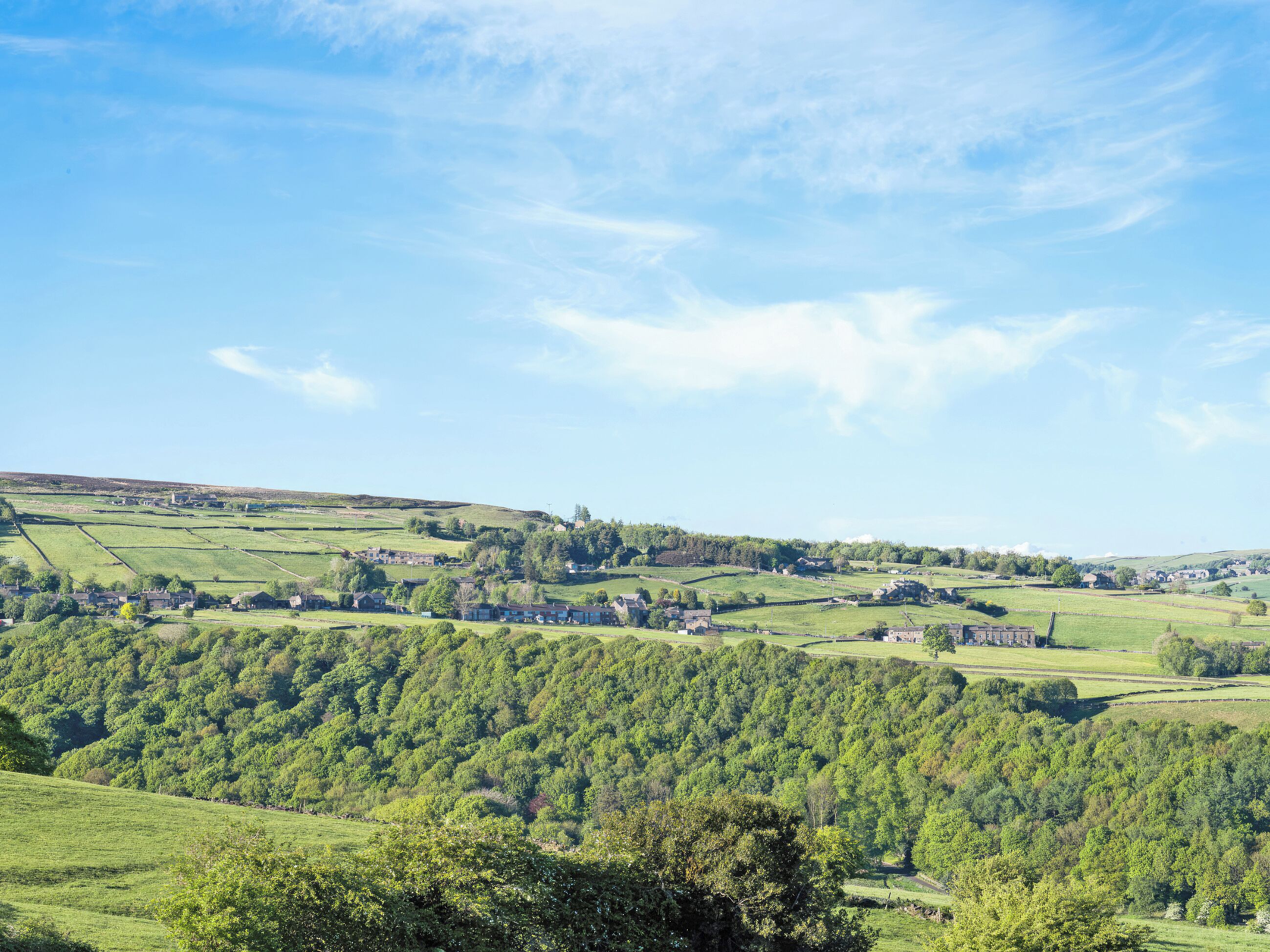 A rural landscape with rolling hills, scattered houses, and a clear sky.