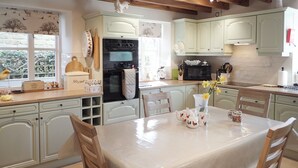 Una cucina con mobili bianchi, un tavolo da pranzo con sedie e una finestra vista alberi.