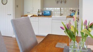 A modern kitchen with white cabinets, a wooden dining table, and a vase with flowers. - 2 bedroom accommodation in Aberystwyth (Aberystwyth)