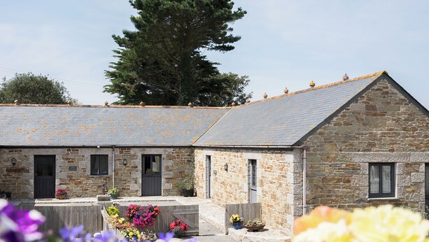 Un bâtiment en pierre avec un toit en tuiles, de nombreuses fenêtres et une clôture en bois ornée de fleurs colorées.