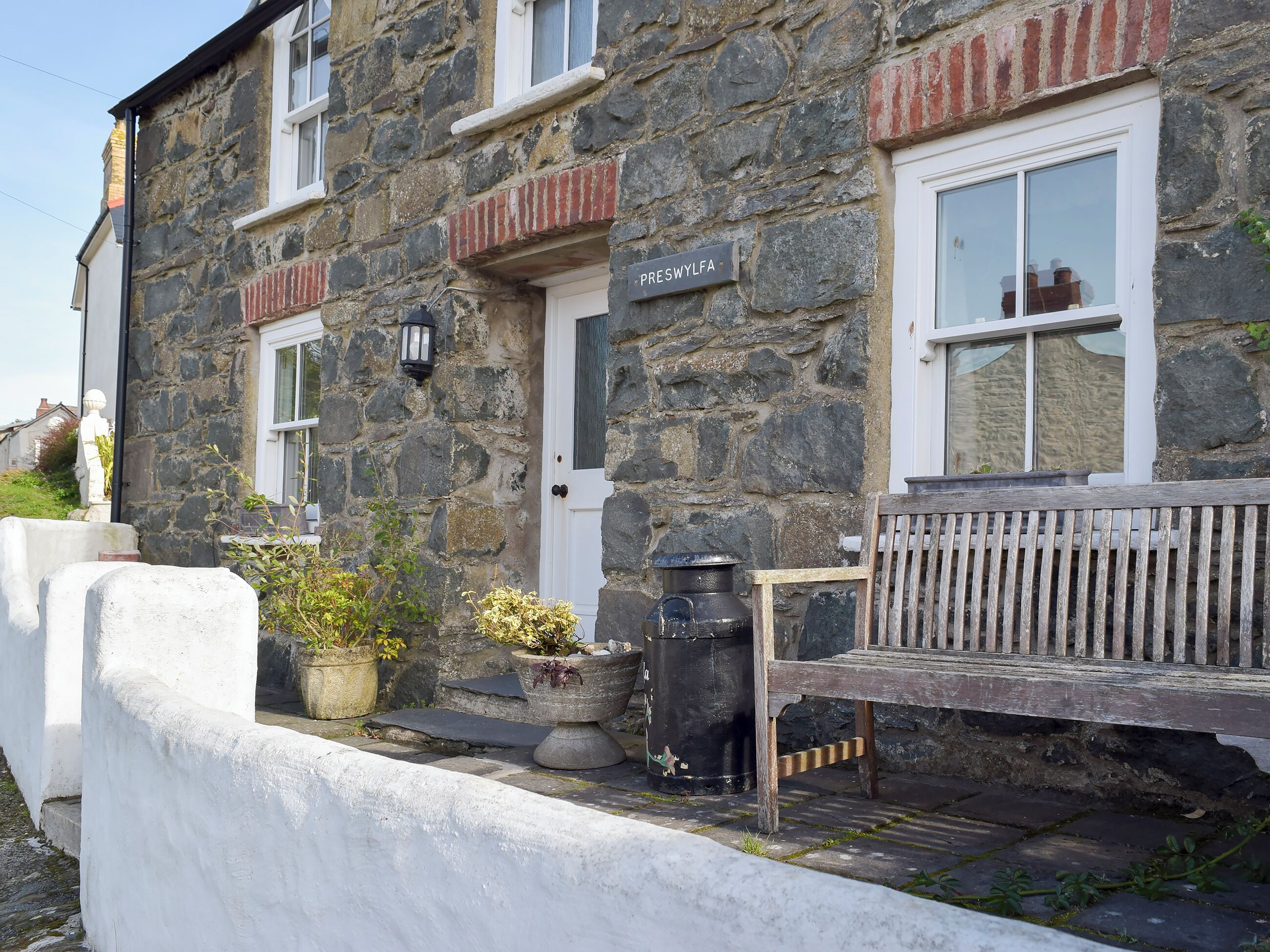 A stone building with a white door labeled "PRESWYLFAN" and a bench outside.