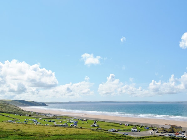 Eine Küstenlandschaft mit Strand, Wiesen und abgestellten Fahrzeugen.