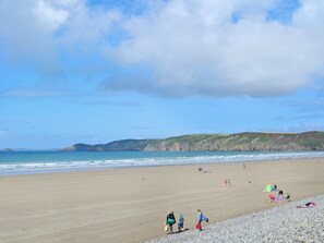 A wide sandy beach with a rocky shoreline, a calm sea, and distant hills under a partly cloudy sky. - 2 bedroom accommodation in Trefin, near St Davids (Trefin, near St Davids)