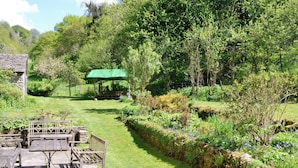 Un jardín con un banco y mesa de piedra, una valla de madera y una estructura de sombrilla verde.