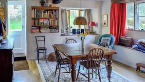 Un comedor con una mesa y sillas de madera, una estantería, una ventana con cortinas y un radiador.