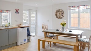 A kitchen with a dining area, wooden furniture, a clock on the wall, and a window with a view of a fence. - 3 bedroom accommodation in Llanarth, near New Quay (Llanarth, near New Quay)