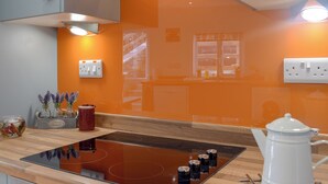 A kitchen with an orange backsplash, a black induction cooktop, a white kettle, and a wooden countertop. - 3 bedroom accommodation in Llanarth, near New Quay (Llanarth, near New Quay)