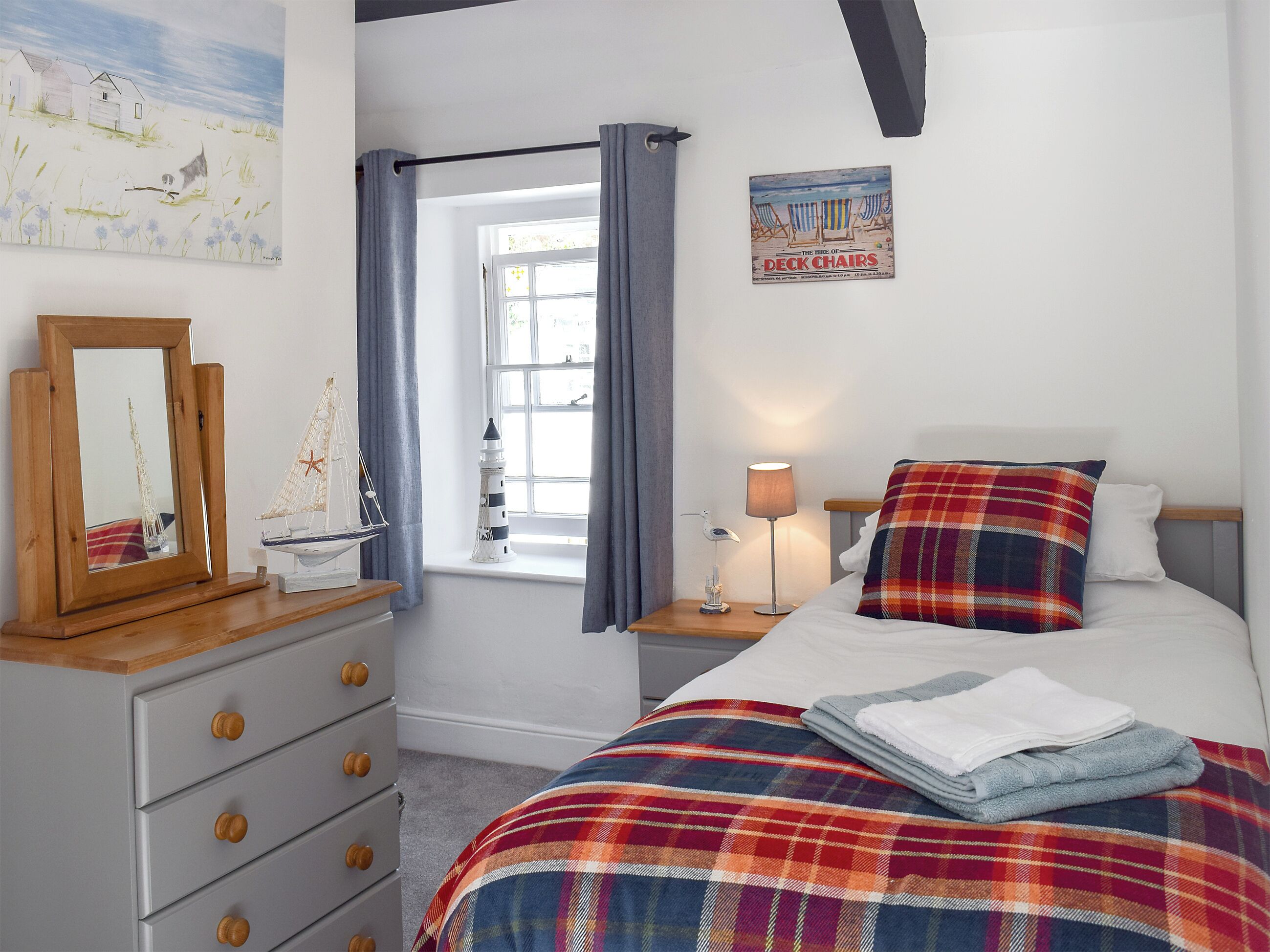 A bedroom with a bed, a nightstand, a dresser, a window with curtains, a painting on the wall, and a poster on the wall.