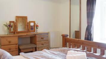 Een slaapkamer met een houten dressoir, een spiegel, een bed met een witte deken en een raam met gordijnen.