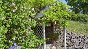 Un jardin agrémenté d’une pergola en bois, de plantes grimpantes et d’un mur en pierre.