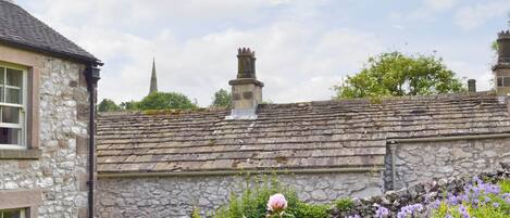 A stone building with a tiled roof, a stone wall, and a garden with flowers.